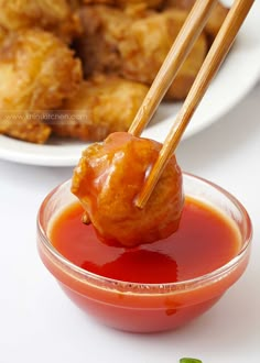 two chopsticks sticking out of a meatball in a small bowl with ketchup