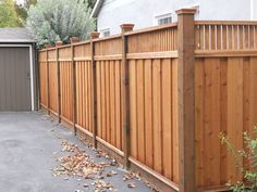 a wooden fence in front of a house with leaves on the ground next to it