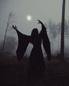 a woman with her arms outstretched standing in the foggy woods at night, holding out her hands to the sun