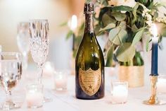 a bottle of champagne sitting on top of a table next to glasses and candles with flowers in the background