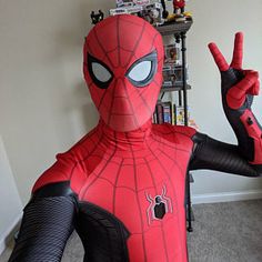 a man in a spiderman costume is making the peace sign with his hand while standing next to a bookshelf