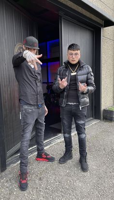 two men standing next to each other in front of a garage door with their hands up