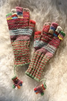 two colorful knitted mittens laying on top of a white furnishing area