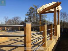 a wooden deck with metal railings and a pergolated area in the background