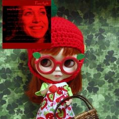 a doll with glasses and a red hat is holding a basket in front of a green wall