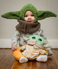 a small child wearing a knitted yoda hat and holding a stuffed star wars toy