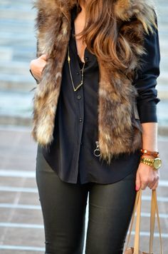 a woman in black shirt and fur vest holding a handbag while standing on the street