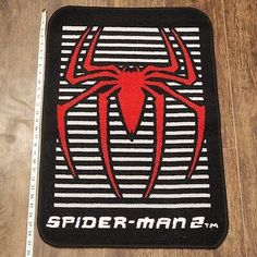 the spider man logo on a black and white striped floor mat with measuring tape next to it