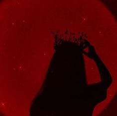 the silhouette of a woman with a crown on her head in front of a red moon