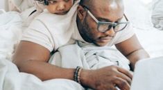 a man laying in bed with a child on his lap looking at a laptop computer