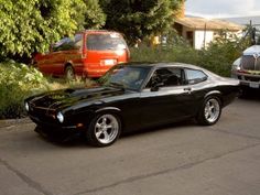 a black muscle car parked in front of a red truck