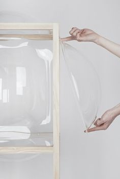 two hands holding a clear plastic bag over a wooden frame with another hand reaching for it