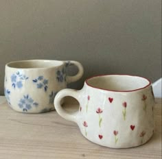 two coffee cups sitting next to each other on top of a wooden table with flowers painted on them