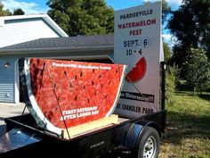 a watermelon festival sign on the back of a trailer in front of a house