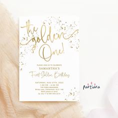 the golden one birthday party card is on top of a white tablecloth with pink flowers