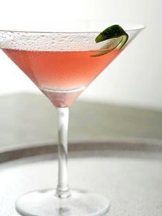 a drink in a martini glass with a lime garnish on the rim and a green leaf