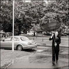 a man holding an umbrella over his head while standing in the rain next to a car