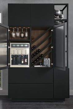 an open cabinet with wine glasses and bottles in it, next to a wall mounted refrigerator