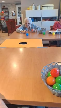 an elderly woman sitting at a table playing with plastic eggs and other colorful balls in a basket