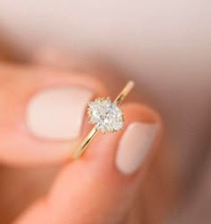 a woman's hand holding an engagement ring with a diamond in front of her