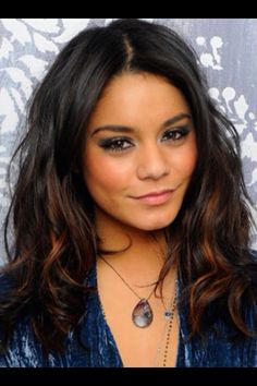 a close up of a person wearing a blue shirt and necklace with an animal print wall in the background