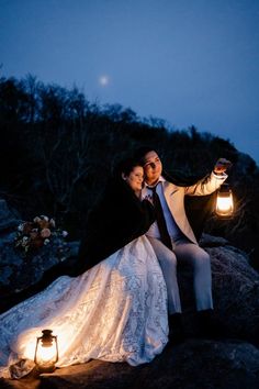 a bride and groom sitting on top of a rock at night with lanterns in the air