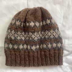 a brown and white knitted hat laying on top of a bed