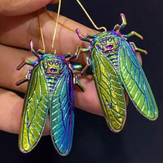 two green and blue insect earrings are being held in someone's hand with gold ear wires