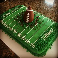 a football themed cake with green frosting on a marble countertop, decorated with grass and sprinkles