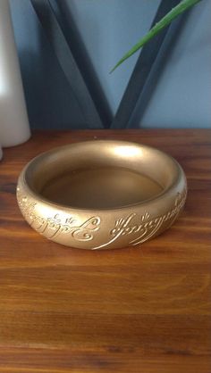 a gold ring sitting on top of a wooden table next to a vase with a plant in it