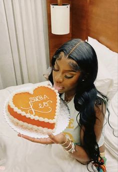 a woman holding a heart shaped cake on top of a bed in front of her face