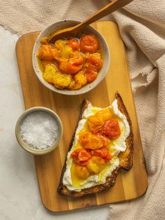 a wooden cutting board topped with bread covered in cheese and tomato toppings next to a bowl of sour cream