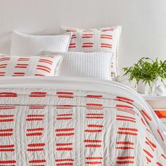 a bed with red and white bedspread, pillows and plants on the side