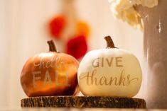 two painted pumpkins sitting next to each other on a table with flowers in the background