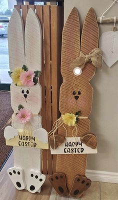 two wooden easter bunnies with bunny ears and flowers on them, hanging from the wall