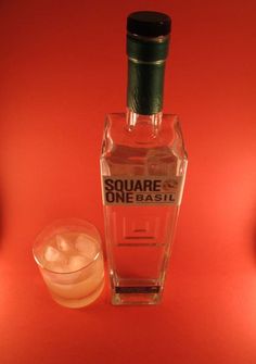 a bottle of liquor sitting next to a glass filled with ice cubes on a red surface