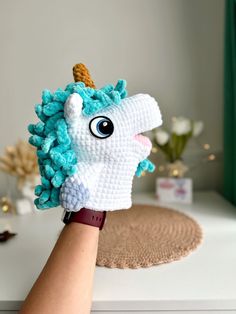 a hand is holding up a crocheted unicorn head