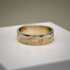 a wedding band with a mountain scene engraved on the side in yellow and white gold