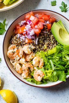 a bowl filled with shrimp, lettuce and tomatoes next to lemon wedges