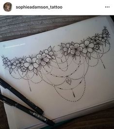 a pen and ink drawing on paper with flowers in the middle, sitting next to some writing utensils