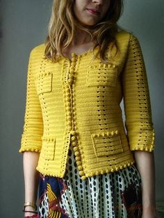 a woman standing in front of a wall wearing a yellow crocheted jacket and skirt