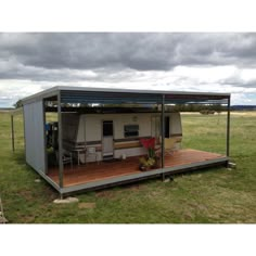 a small mobile home in the middle of a grassy field with a covered porch and picnic table