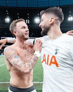 two men standing next to each other in front of a soccer field with lights on