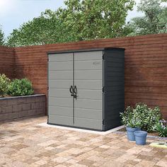 an outdoor storage shed in the middle of a brick patio with potted plants on either side