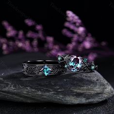 two silver rings with blue topazte and green crystal stones on a rock in front of purple flowers