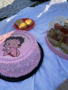 a pink cake sitting on top of a table next to bottles of alcohol and cookies