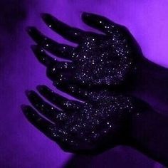 a person's hand with black glitter on it in front of a purple background