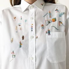 a close up of a person wearing a white shirt with colorful embroidered designs on it