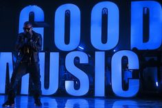 a man standing on top of a stage next to a blue neon sign that says good music