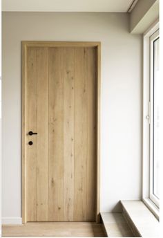 a wooden door sitting next to a window in a white walled room with wood flooring